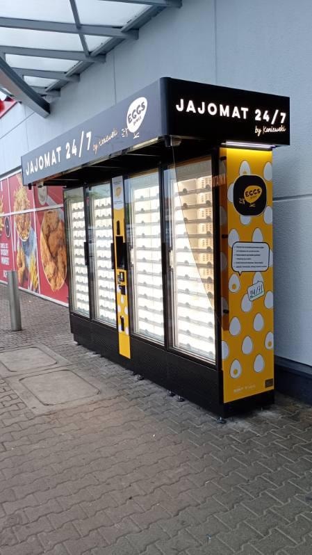 Yellow egg vending machine under a canopy beside a shop